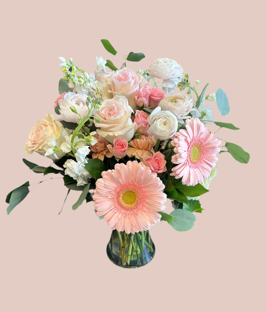 Soft blend of blush and ivory in roses, stock, ranunculus, spray roses in a medium vase. 