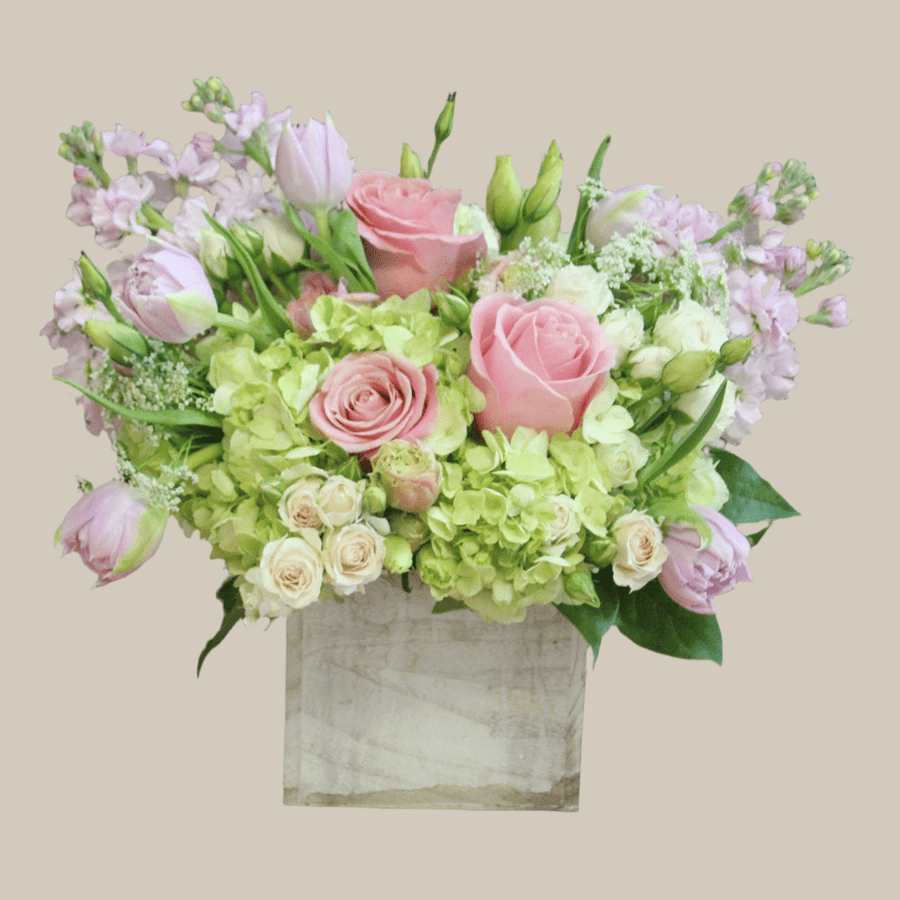 Spring bouquet with pink roses, lilac tulips, lisianthus, blush spray roses, green hydrangeas, lilac stock in a wooden cube.