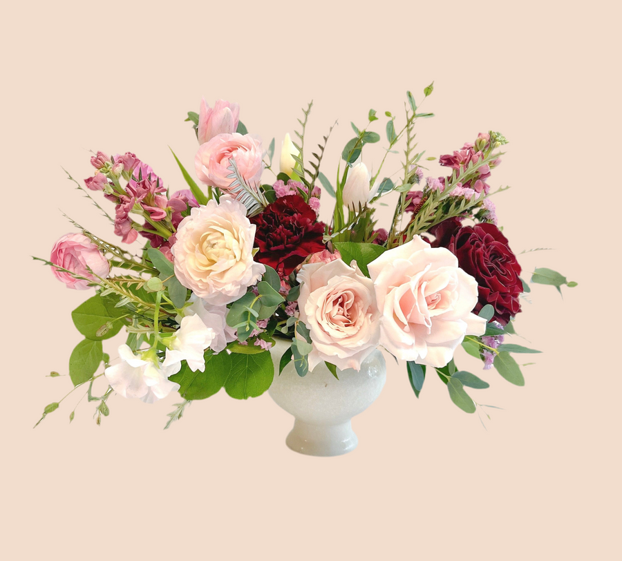 Red garden roses, ivory roses, blush ranunculus, stock, sweet pea, seasonal Valentine flowers in a white ceramic vase ready for delivery in Houston. 