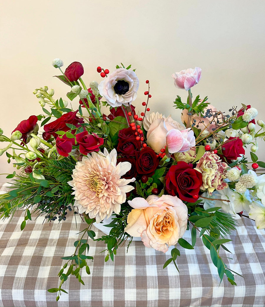 Garden style Christmas centerpiece with shimmering roses, peach dahlias, white anemones, red spray roses, white delphiniums, ilex and hypericum berries, red ranunculus, Christmas foliage in a ceramic vase. Bring the Christmas spirit to Houston for birthdays, anniversary, get well soon, Christmas party. Delivery and pickup in Houston.