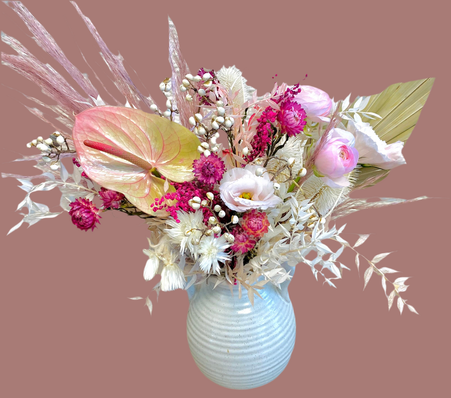  Modern valentine arrangement: dried palm leaf, mauve pampas grass, vibrant hot pink dried strawflower, soft pink lisianthus, pink ranunculus, dried tallow berries, and preserved ruscus in a white ceramic vase