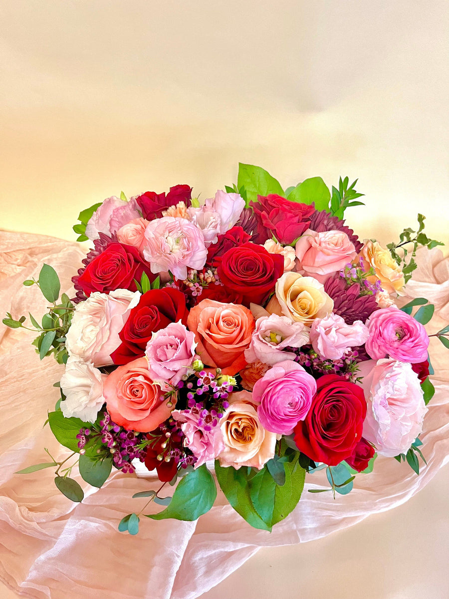 Valentine arrangement featuring red roses, coral roses, peach roses, pink ranunculus, hot pink ranunculus, pink lisianthus, waxflower in a wooden box.
