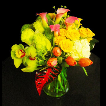Tropical flowers orchids, green roses, bicolored calla lilies and yellow spray roses in a concave vase, birthday flowers.