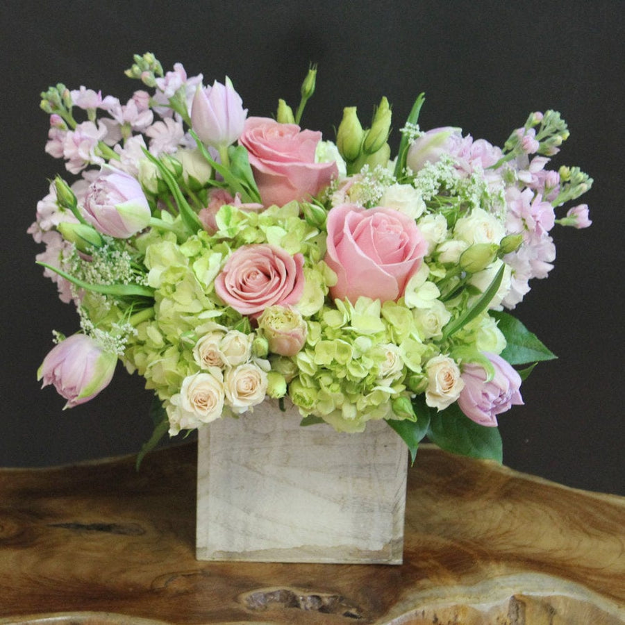 Hermosa pink roses, lilac tulips, lisianthus, blush spray roses, green hydrangeas, lilac stock in a wooden cube.