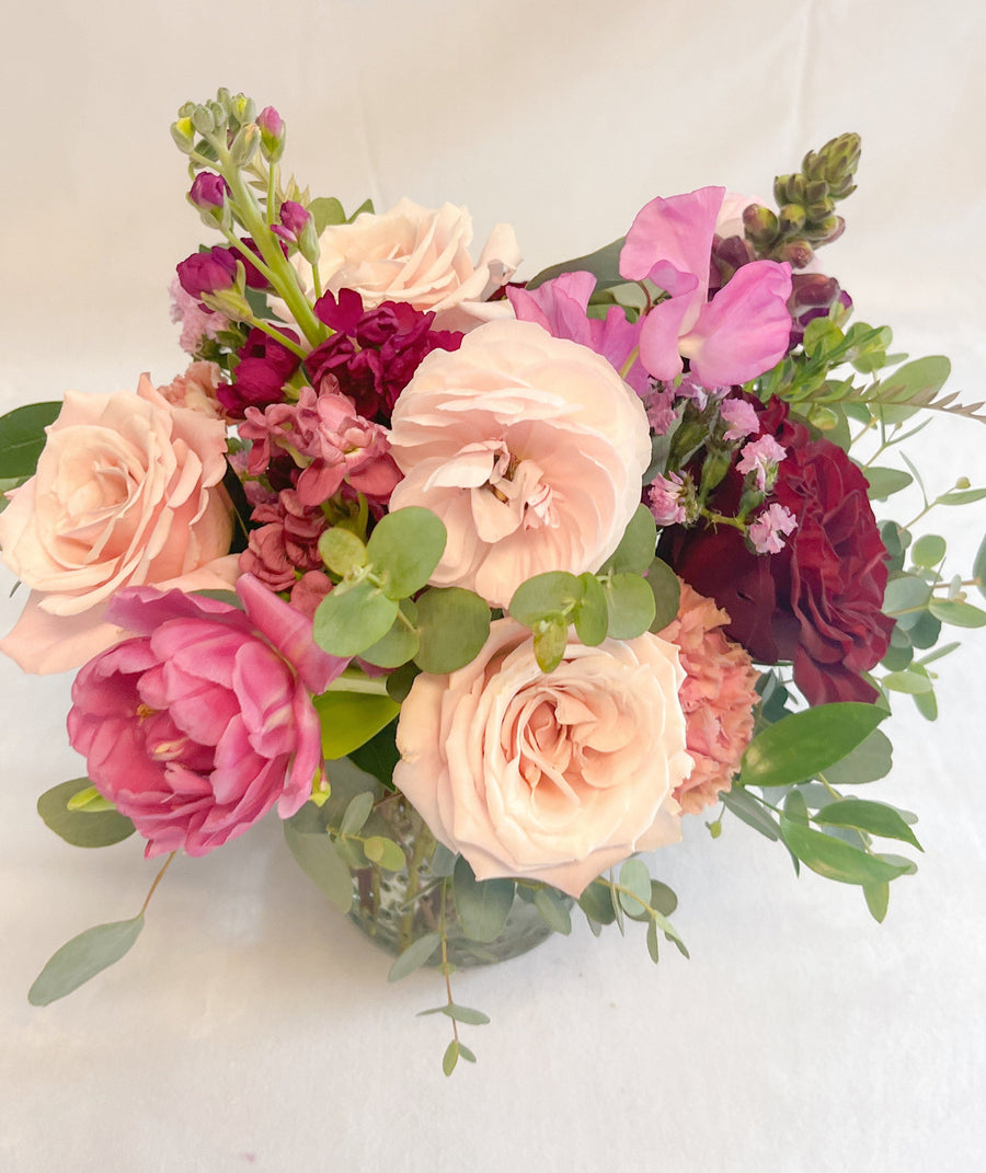 Small Valentine Arrangement made seasonal blooms like roses, spray roses, ranunculus, stock in a clear vase. 