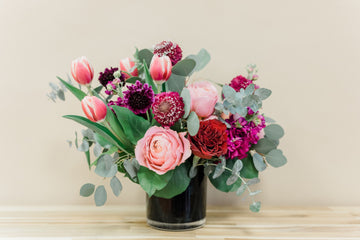 Valentine flowers like garden roses, scabiosa pods, tulips, stock, and eucalyptus greenery, elegantly arranged in a black cylinder vase. Same day delivery across Houston