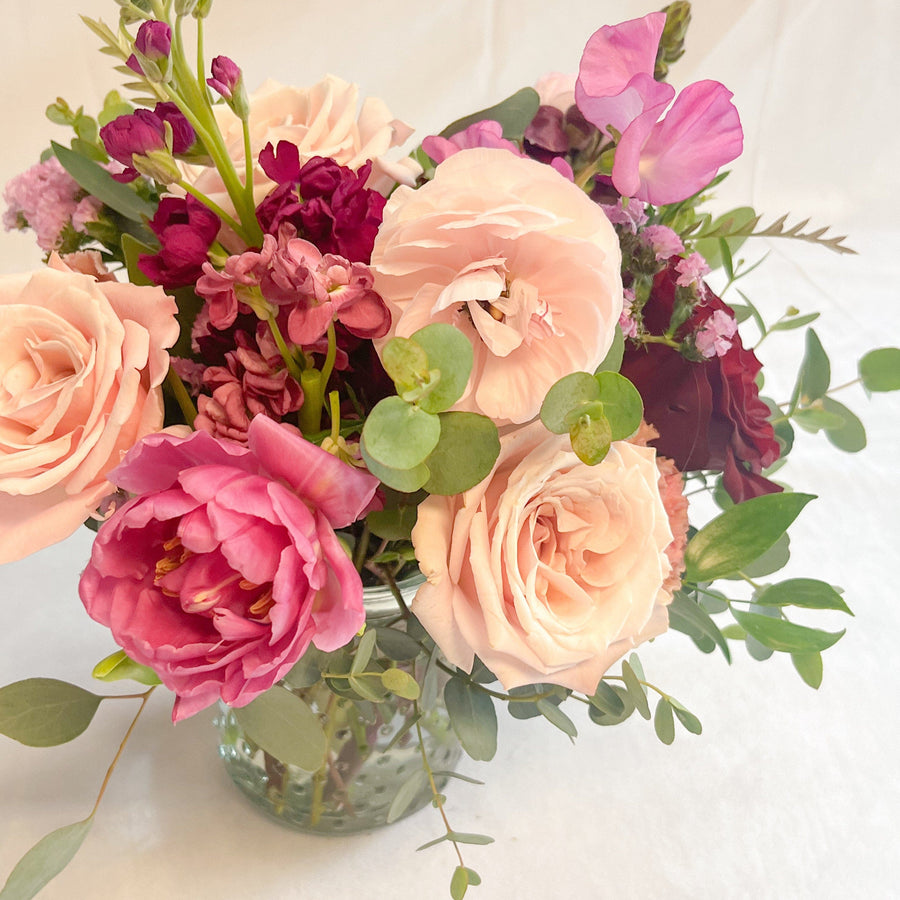 Seasonal valentine flowers and premium blooms, roses, ranunculus, spray roses, stock, sweet pea and greenery in a clear vase. Valentine gift ready for delivery or pick up in Houston. For any occasion birthdays, anniversary, get well soon, or just because.